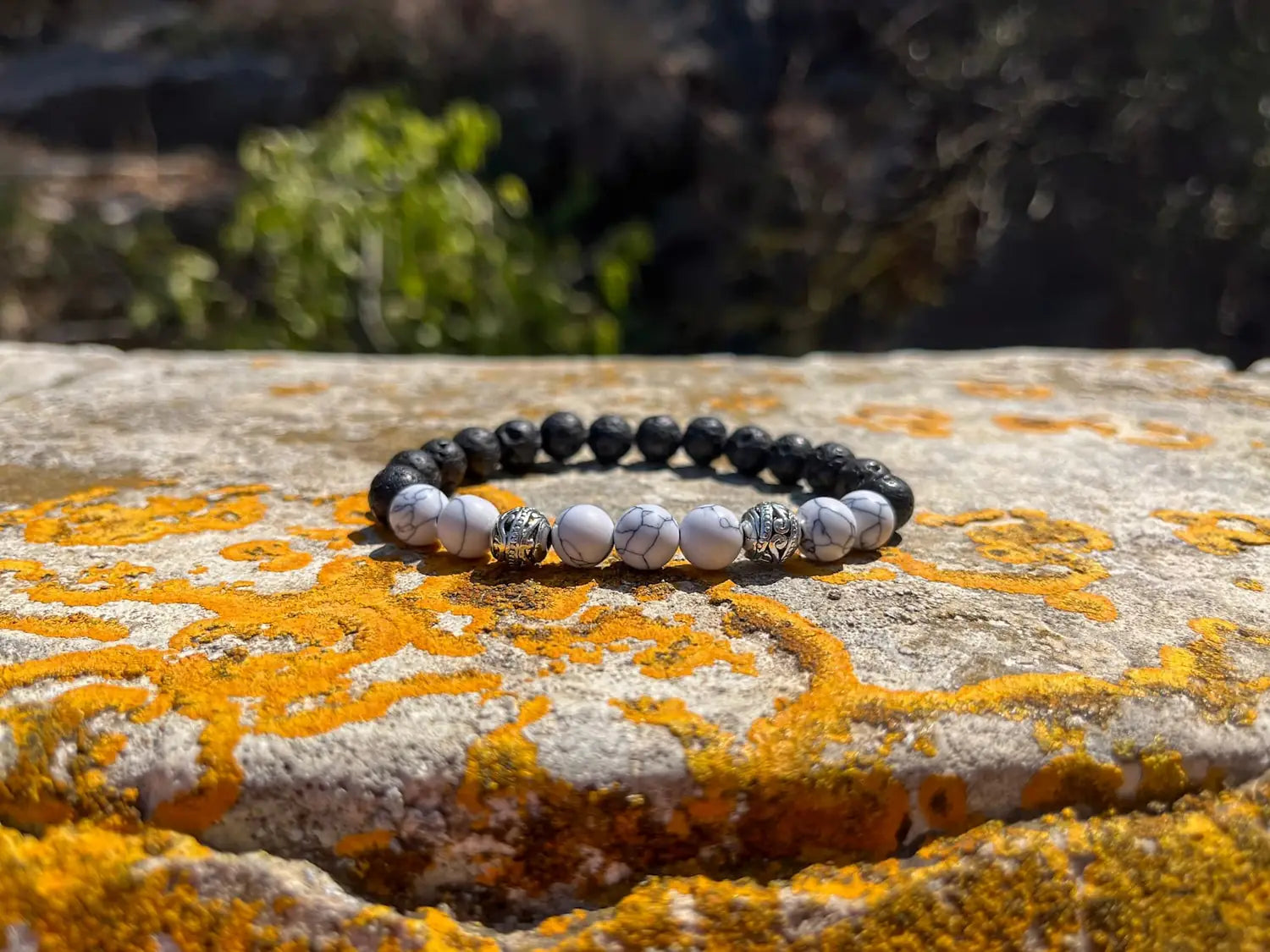 Perlenarmband aus Lava- und Howlithsteinen auf sonnenbeschienener Felsoberfläche.