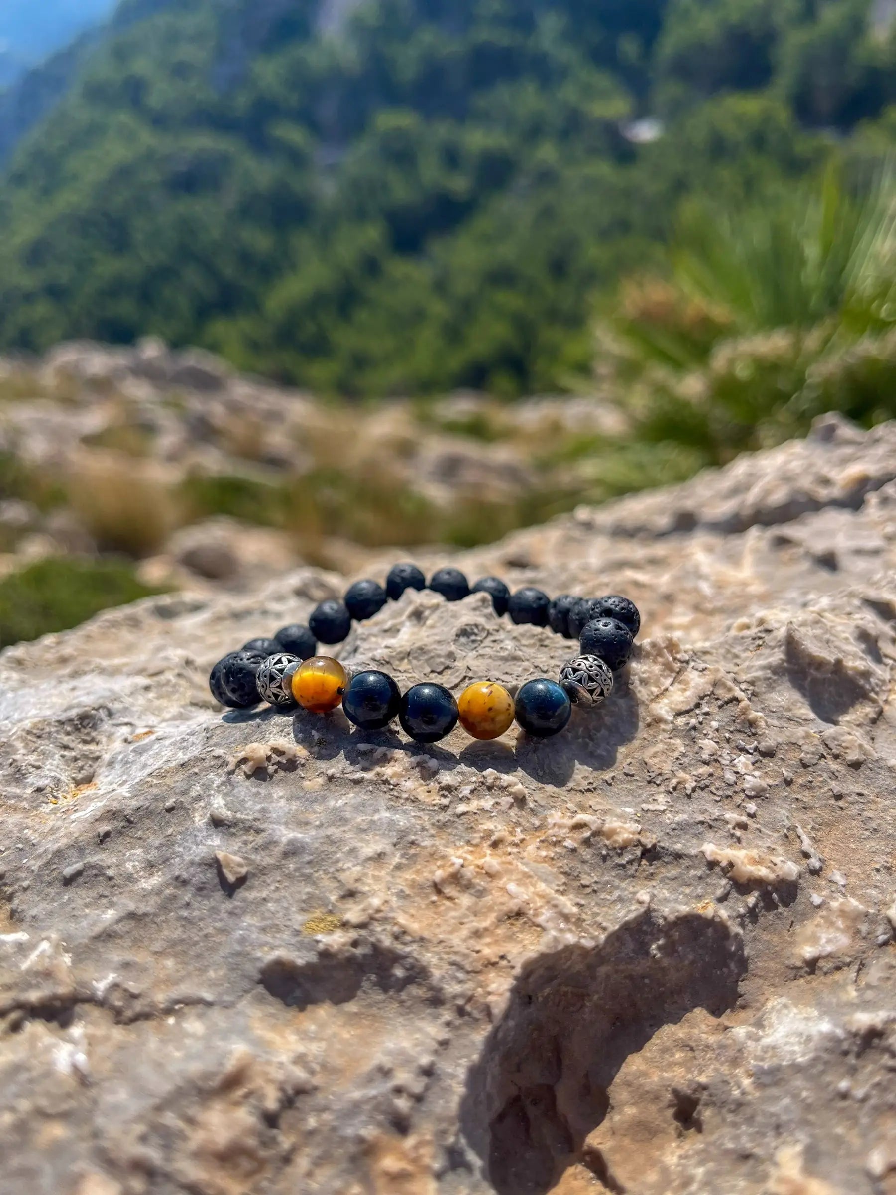 Perlenarmband aus Natursteinen auf einem sonnenbeschienenen Felsen mit Landschaft im Hintergrund.